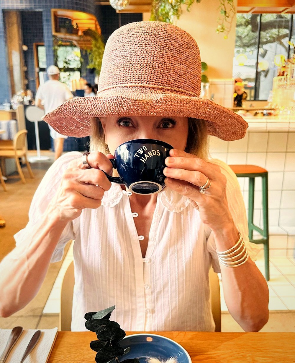 Rhonda Evans in a straw hat, drinking from a navy Two Hands cup in a café.
